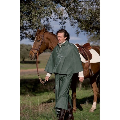 Homem com capa e calças impermeáveis verdes segurando rédea de cavalo castanho com sela branca e castanha em área gramada