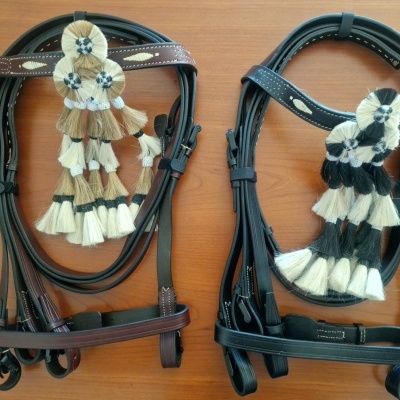 Duas rédeas de couro com enfeites de tecido pretos e brancos sobre madeira