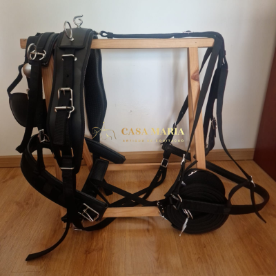 Cabresto e rédea pretos com fivelas metálicas pendurados num suporte de madeira clara