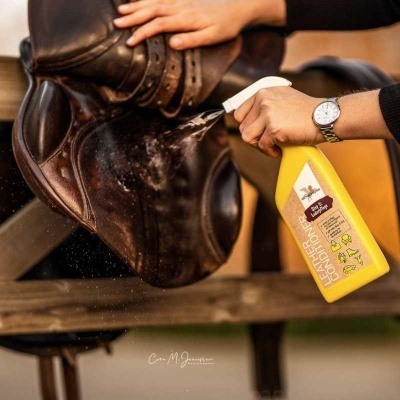 Pessoa a limpar sela de couro castanho com spray amarelo EQUIMAN CONDITIONER