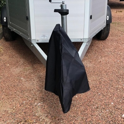 Reboque cinza com suporte metálico coberto por capa preta em terreno de cascalho