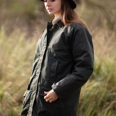 Mulher de casaco verde-escuro e chapéu castanho com padrão xadrez ao ar livre