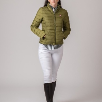 Mulher a usar casaco acolchoado verde oliva com fecho de correr, camisa às riscas, calças brancas e botas pretas.