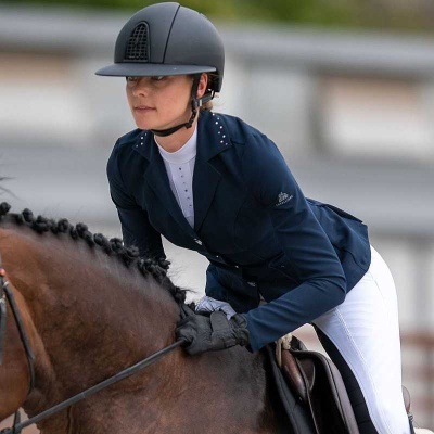 Cavaleira com roupa de equitação azul e branca e capacete preto a montar cavalo castanho