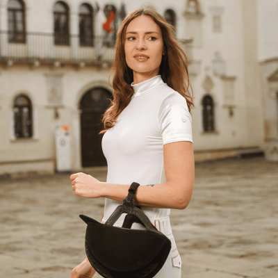 Mulher com camisa branca de manga curta e capacete preto de equitação em cenário urbano histórico