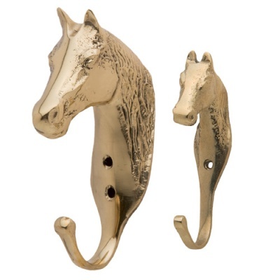 Dois ganchos metálicos dourados em forma de cabeça de cavalo em fundo branco.