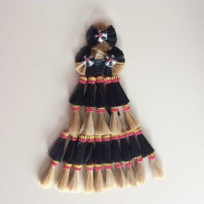 Trança decorativa com fios naturais bege e preto, amarrada com fios vermelhos e dourados.