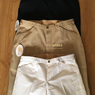 Três calças de equitação azul escuro, bege e branco sobre fundo de madeira clara