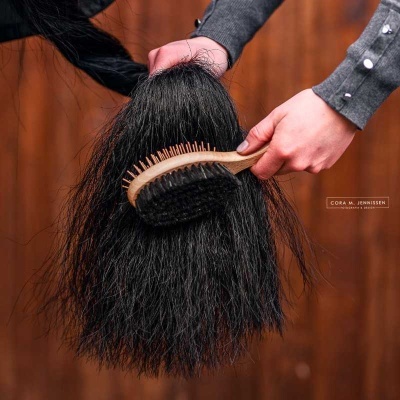 Escova de madeira com cerdas pretas a pentear cabelo grosso preto em fundo de madeira marrom