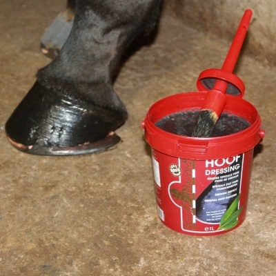 Pote vermelho de Hoof Dressing com escova junto ao casco de cavalo