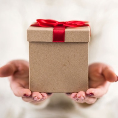 Caixa de presente castanha com fita vermelha nas mãos