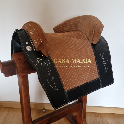 Sela equestre castanha e preta com padrões acolchoados e bordados branco num suporte de madeira