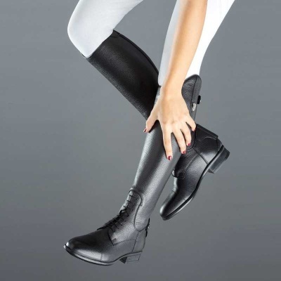 Bota de equitação preta com calças brancas num fundo cinzento.