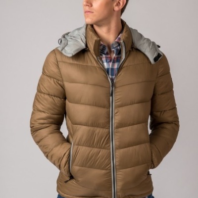 Casaco acolchoado castanho com capuz cinzento e fecho de correr, camisa xadrez e jeans azuis