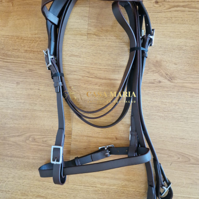 Cabresto castanho de pele com fivelas metálicas sobre chão de madeira clara com texto CASA MARIA