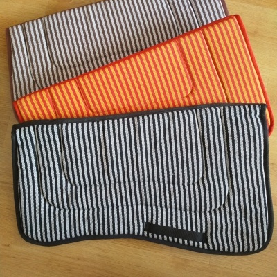 Três mantas de cavalo listradas em diferentes cores sobre pavimento de madeira clara