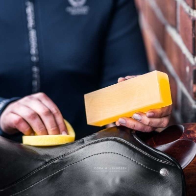 Pessoa a limpar sela de couro preto com esponja amarela e bloco sólido amarelo