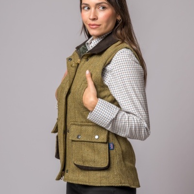 Colete feminino verde oliva com bolso frontal e gola castanha, usado com camisa xadrez e calças pretas