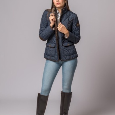 Mulher de pé com casaco acolchoado azul escuro, jeans e botas castanhas altas