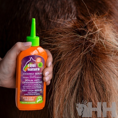Frasco laranja de sérum anti-comichão Equi natura com tampa verde junto a pelo castanho grosso
