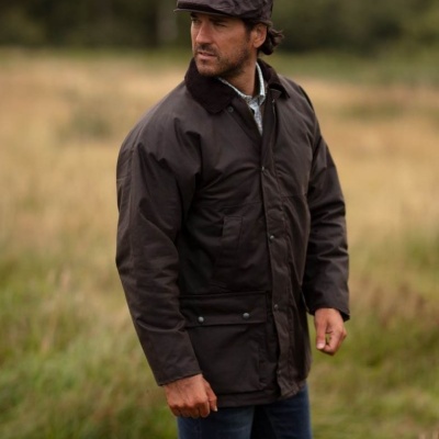 Homem com casaco castanho, calças azuis e boina castanha em campo com relva