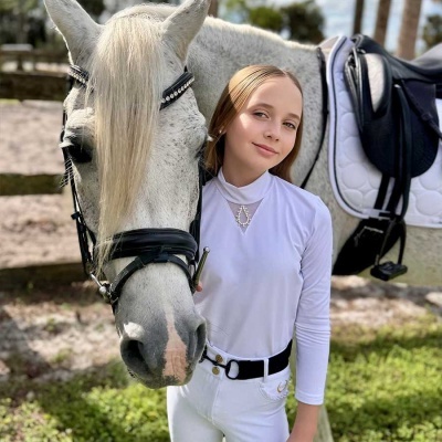 Rapaziada com roupa de equitação ao lado de cavalo branco com sela.