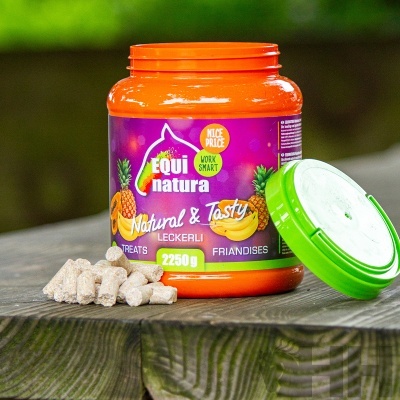 Frasco laranja com tampa verde e rótulo roxo contendo snacks para cavalos EQUInatura Natural & Tasty, sobre mesa de madeira