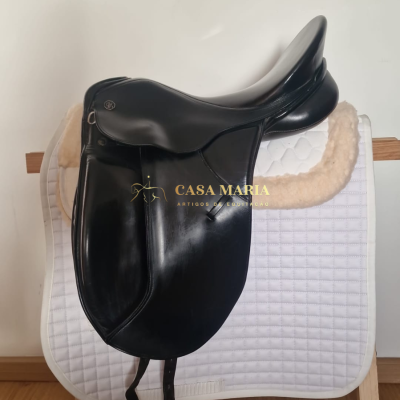 Sela de equitação preta em couro sobre manta branca acolchoada em suporte de madeira.