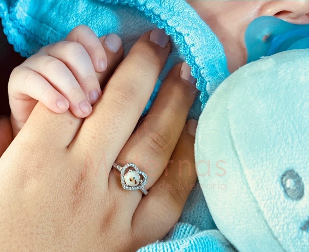 Anel Coração Alto Mão de adulto com anel de ursinho em coração segurando mão de criança com mantinha e chupeta azul
