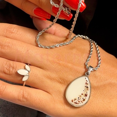 Colar prata com pingente branco e castanho sobre mão com unhas vermelhas