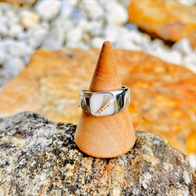 Anel prateado com detalhe decorativo branco e amarelo em suporte de madeira cónica