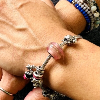 Pulseira com contas decorativas em metal e rosa em pulso, com outro pulso com pulseiras de contas coloridas