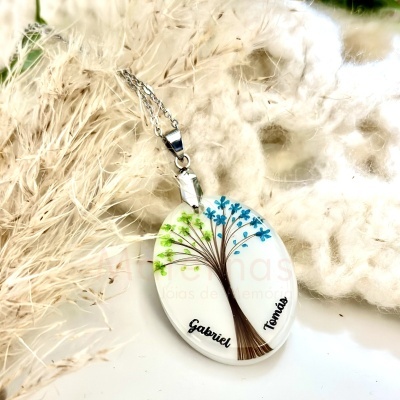Colar pendente oval branco com árvore e nomes, em fundo de fibras naturais e tecido macio.