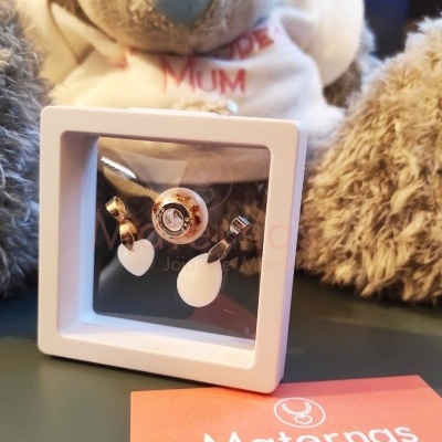 Conjunto de brincos dourados com gotas brancas numa caixa branca sobre mesa verde com peluches