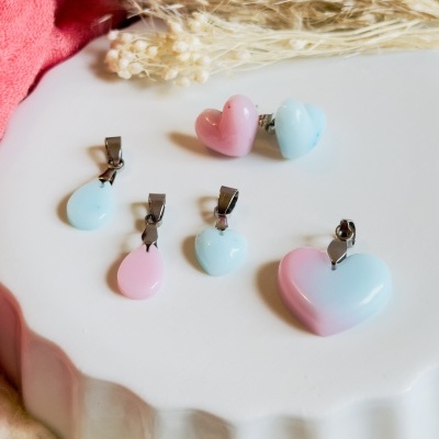 Conjunto de brincos e pendentes em forma de coração e lágrima em azul e rosa pastel sobre superfície branca