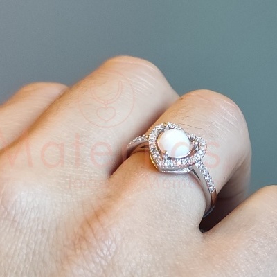 Anel prateado com pérola branca central e brilhantes num dedo