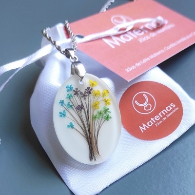Colar com pendente oval branco com flores coloridas em saco branco com marca Maternas