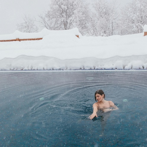 Mulher numa piscina exterior cercada por neve e árvores nevadas