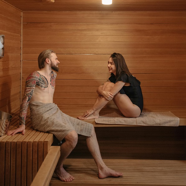 Interior de sauna com duas pessoas sentadas em bancos de madeira clara
