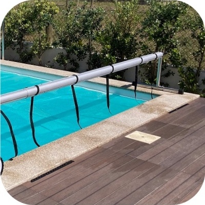 Cobertura de piscina enrolada com correias pretas e estrutura metálica ao lado de piscina