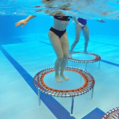 Trampolins pequenos subaquáticos numa piscina com duas pessoas a saltar.