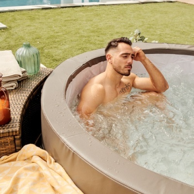 Homem num jacuzzi ao ar livre com vasos decorativos e mantas próximas