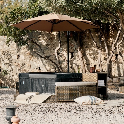 Conjunto de mobiliário exterior com poltrona em rattan e guarda-sol castanho junto a parede de pedra