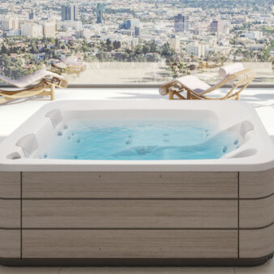 Banheira de hidromassagem quadrada com revestimento em madeira e água azul numa varanda com vista urbana e espreguiçadeiras.