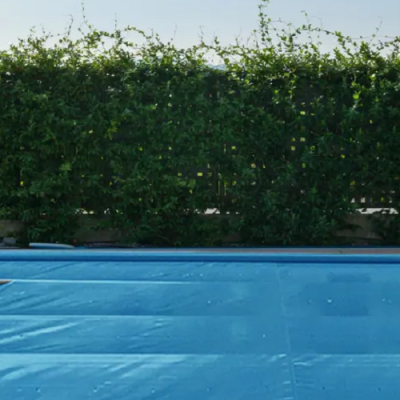 Cobertura azul para piscina com cerca metálica e vegetação verde ao fundo