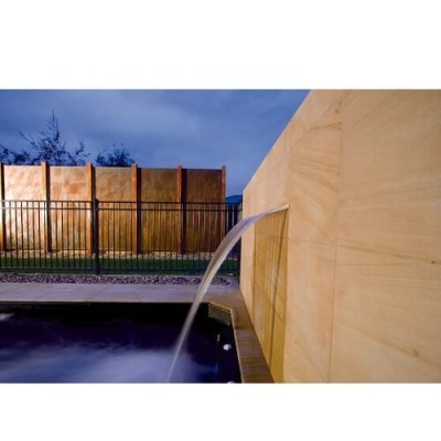 Fonte de água em parede de pedra a cair em piscina, com grades e painéis metálicos ao fundo.