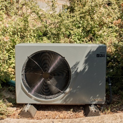 Unidade exterior de ar condicionado cinzenta com ventoinha circular e vegetação ao fundo