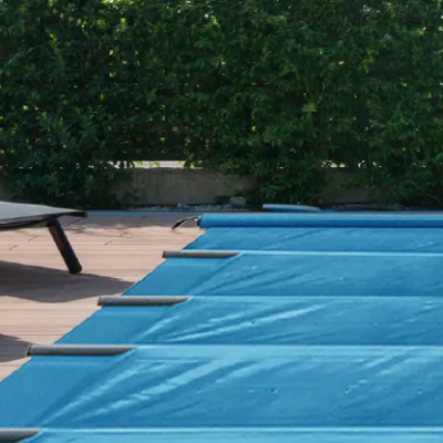 Capa azul para piscina com tiras pretas e fundo de chão em madeira e sebes verdes