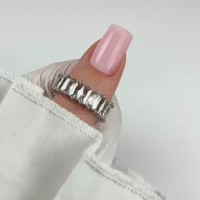 Anel prateado com pedras retangulares em dedo com unha rosa