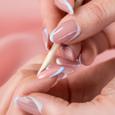 Unhas com manicure em nude, azul claro e branco, com aplicador de madeira perto